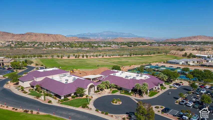 Expansive clubhouse featuring a multi-wing architectural design, metal roofing, paved circular drop-off area, adjacent parking lot, and mountain scenery
