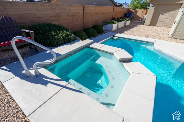 In-ground spa with stone tile accents, swimming pool, concrete deck, gravel landscaping, and concrete block perimeter wall