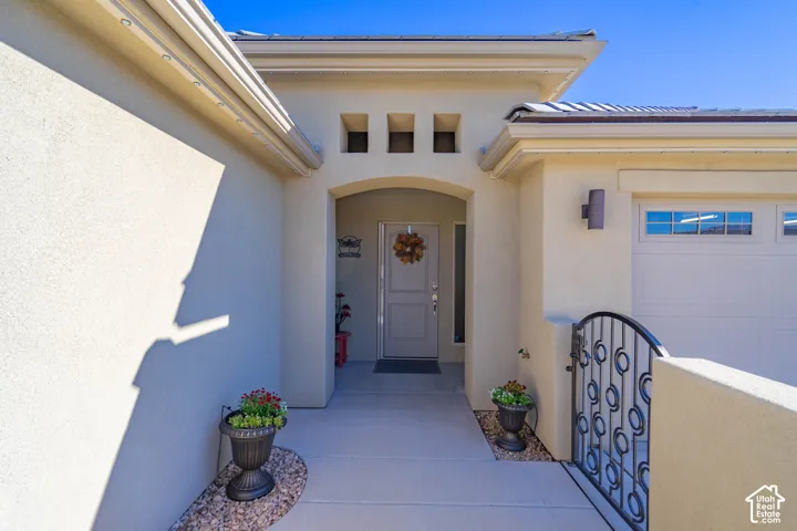 Stucco exterior entry featuring a recessed doorway, triple-niche accent window, attached sectional garage door, and decorative wrought iron gate