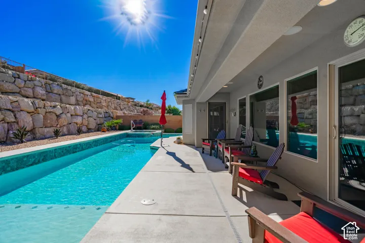 Outdoor area featuring a rectangular in-ground swimming pool, concrete patio, recessed exterior lighting, and natural stone retaining wall