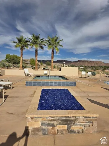 Outdoor patio featuring a built-in fire feature with cobalt blue glass, raised spa with tiled surround, and a concrete deck with a mountain backdrop