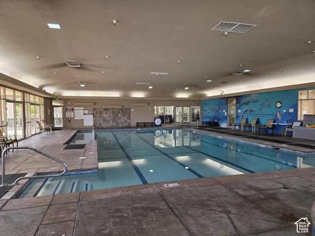 Indoor swimming pool featuring multiple lap lanes, tiered entry steps, stone tile decking, recessed lighting, and wall-mounted water shower fixtures