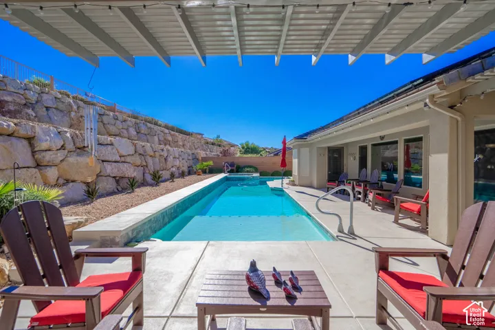 In-ground swimming pool with concrete patio, covered patio area, and tiered natural stone retaining wall