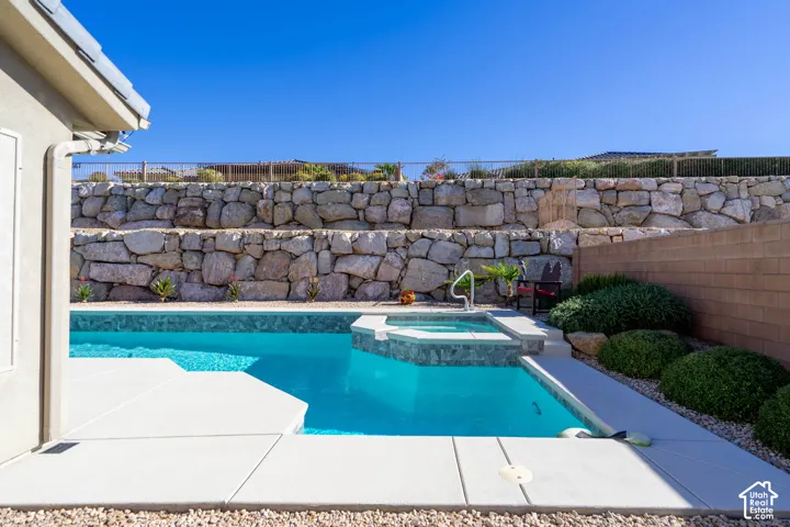 In-ground swimming pool with an integrated spa, concrete deck, terraced stone retaining walls, and rock landscaping