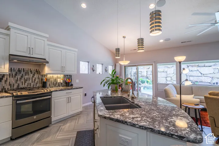 Kitchen featuring stone-finish countertops, a central island with an undermount dual-basin sink, herringbone-pattern flooring, stainless steel appliances, and a mosaic tile backsplash