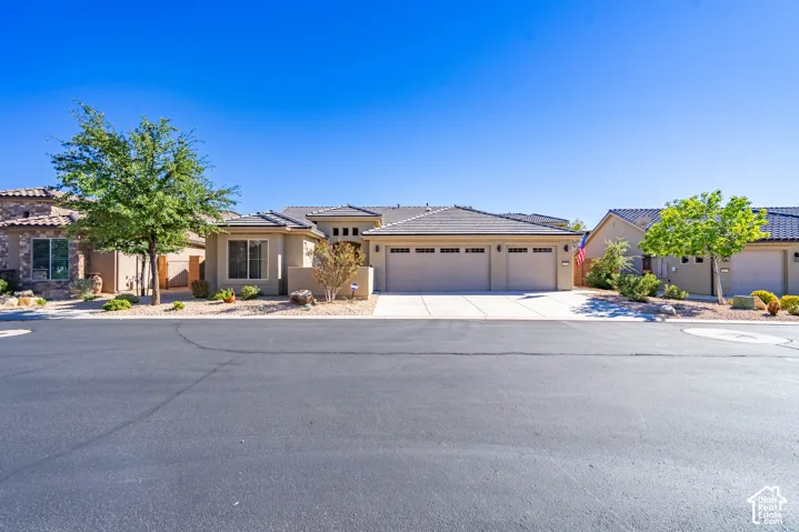 Single-story exterior featuring a stucco facade, tile roof, three-car garage, and desert-inspired landscaping