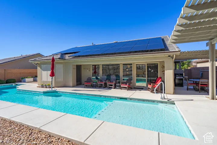 Private saltwater swimming pool with a tanning ledge and concrete decking, integrated roof-mounted solar panels, and a pergola-covered patio