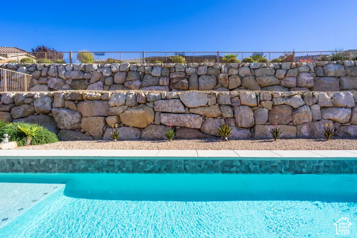 Swimming pool featuring tiled coping and light-toned surfacing, backed by a multi-tiered natural stone retaining wall and metal perimeter fencing