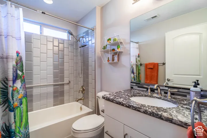Bathroom featuring a vanity with a stone-patterned countertop, an undermount oval sink, chrome dual-handle faucet, full-width mirror, and a shower-tub combination with vertically patterned tile surround