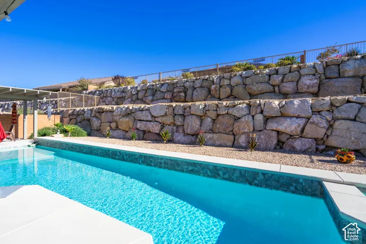 Swimming pool with stone-tiled edge, multi-tiered natural stone retaining wall, and gravel landscape surround