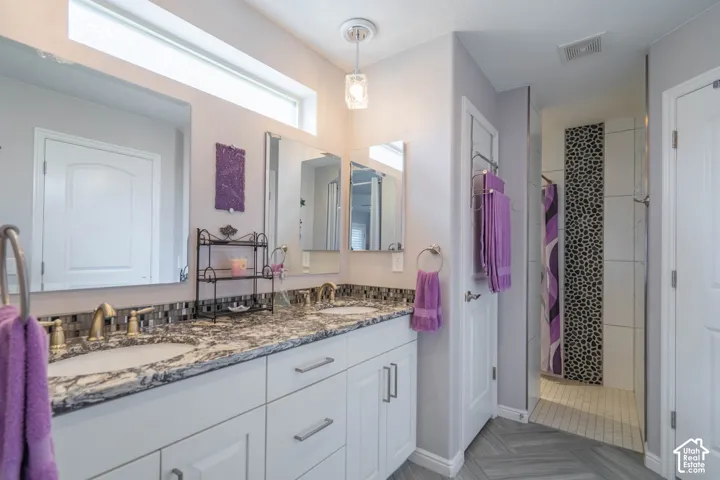 Double vanity with stone-patterned countertops, dual undermount sinks, custom mosaic tile backsplash, pendant lighting, and herringbone-patterned flooring