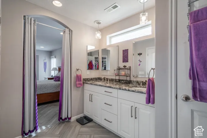 Dual-sink vanity with stone countertop and white cabinetry, complemented by chevron-patterned flooring, arched entryway, and dual hanging pendant lights