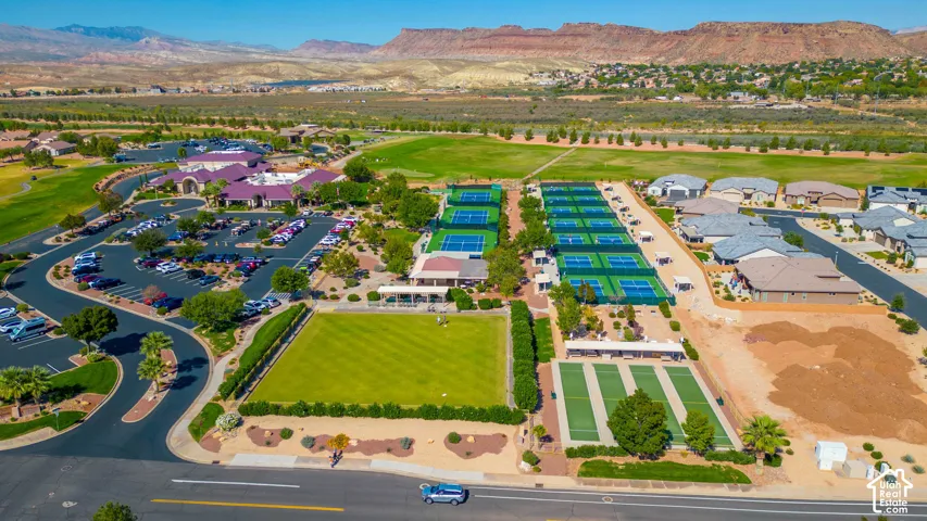Aerial perspective of community recreation grounds featuring multiple tennis courts, pickleball courts, a manicured lawn, and expansive mountain terrain