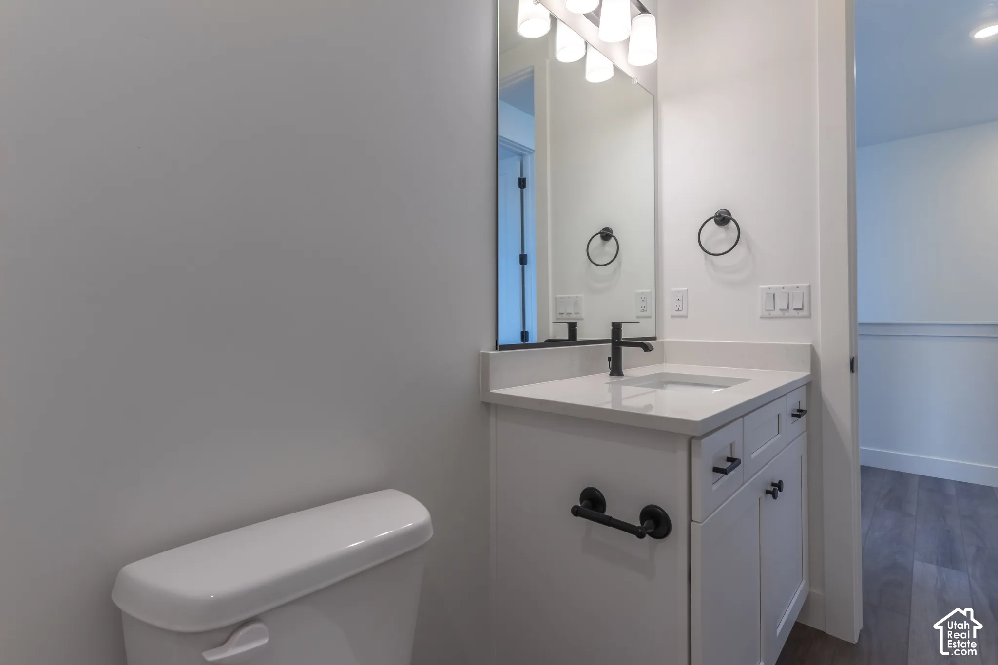 Bathroom vanity featuring white cabinetry, a light-toned solid surface countertop with an integrated rectangular sink, matte black hardware, and a multi-bulb light fixture