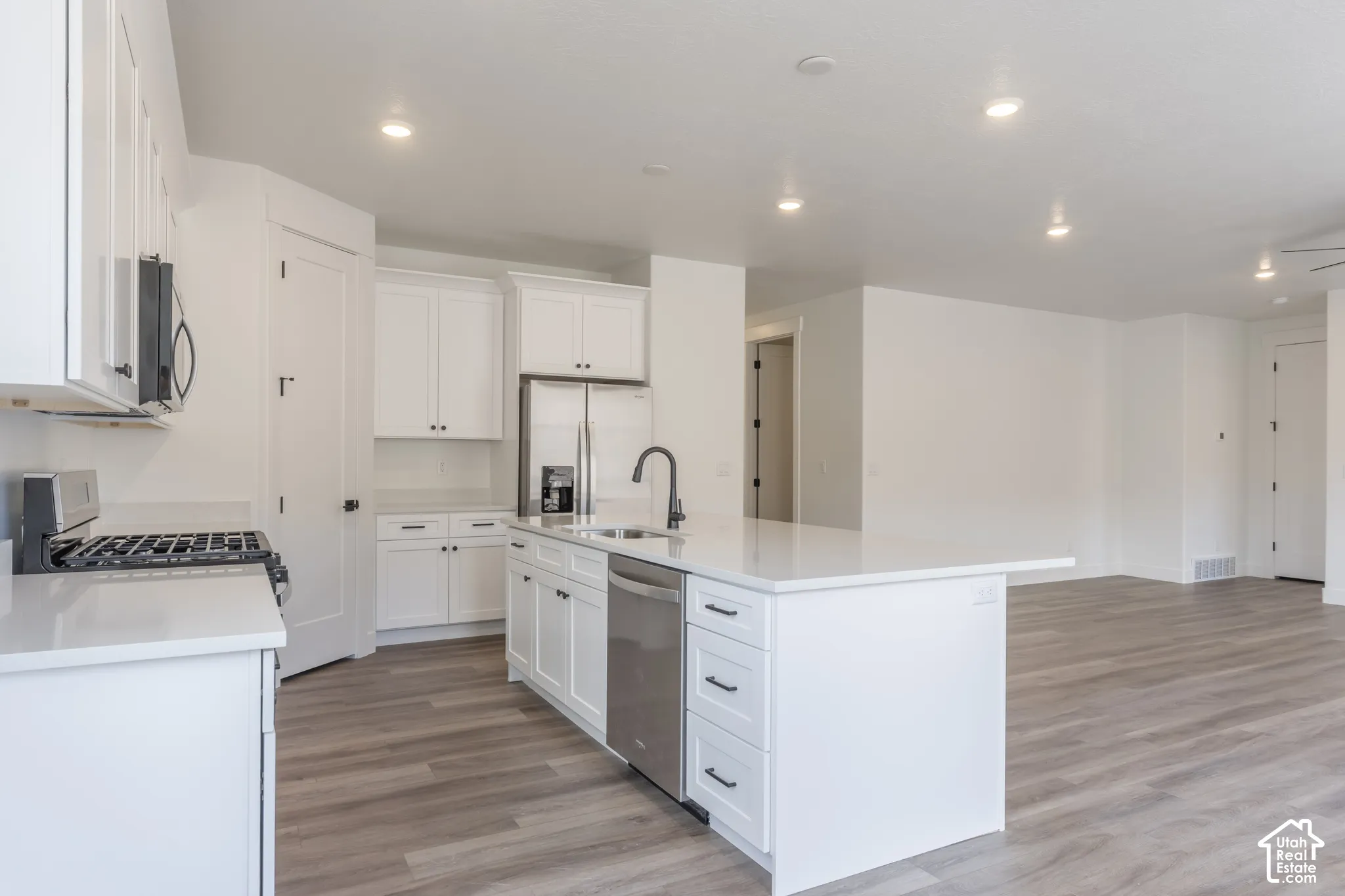 Kitchen featuring white cabinetry, solid surface countertops, a central island with an integrated stainless steel dishwasher, wood-finish flooring, and recessed ceiling lighting