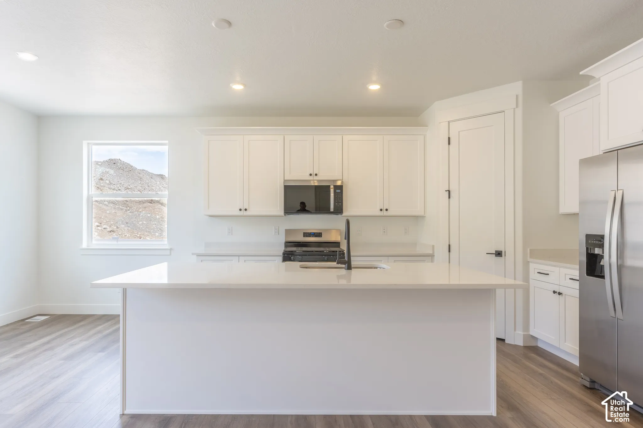 Kitchen featuring a quartz-topped center island, white shaker-style cabinetry, stainless steel appliances, and wood-finish flooring