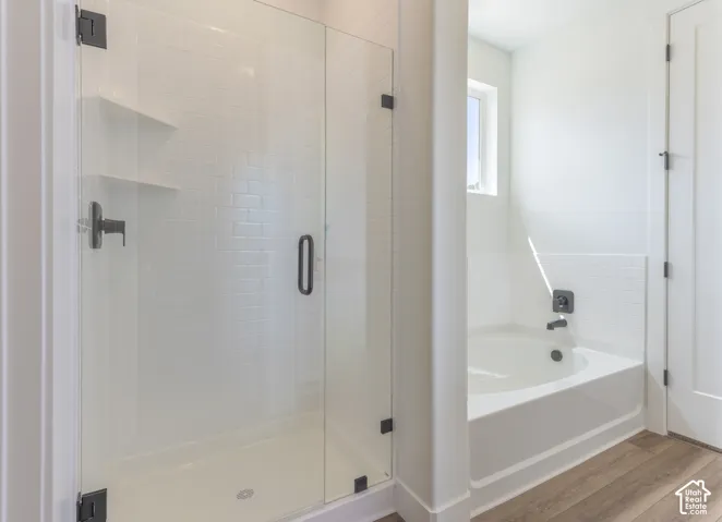 Walk-in shower with white subway tile, integrated shelving, and a frameless glass door, paired with a deep soaking tub featuring matching matte black fixtures and wood-finish flooring