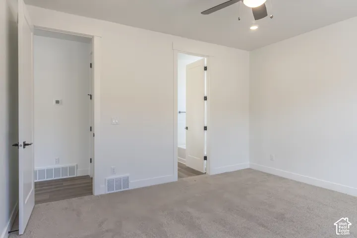 Neutral-toned carpeted bedroom featuring a ceiling fan with integrated lighting, solid-core doors with matte black hardware, and wood-finish flooring in the walk-in closet