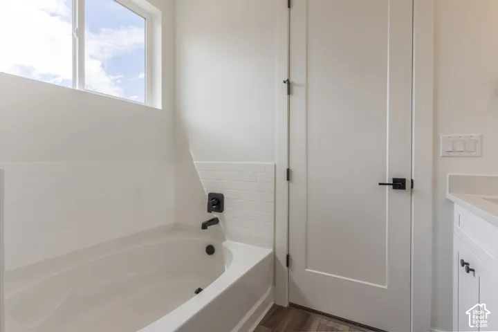 Deep-basin soaking tub featuring a white subway tile surround, matte black plumbing fixtures, wood-finish flooring, and a single-panel interior door with matte black hardware