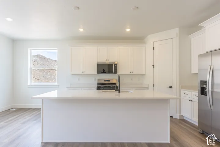 Kitchen featuring a quartz-topped center island, white shaker-style cabinetry, stainless steel appliances, and wood-finish flooring