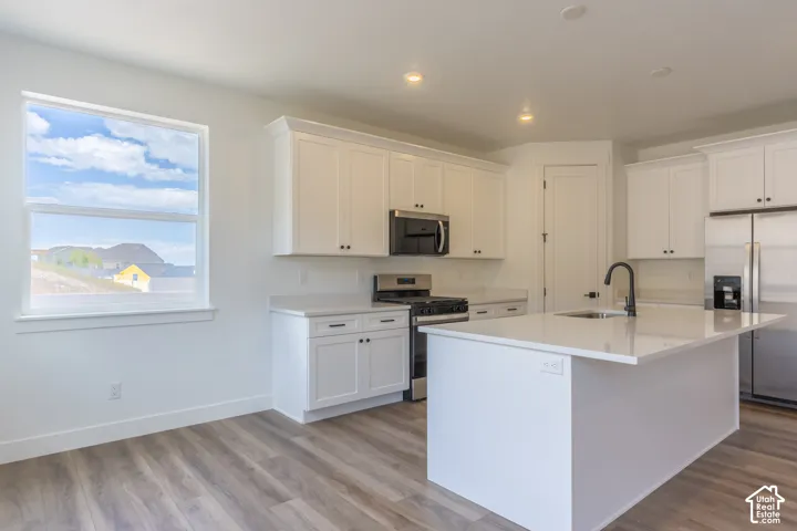 Kitchen featuring white shaker-style cabinetry, quartz countertops, a central island with a matte black faucet, stainless steel appliances, and wood-finish flooring