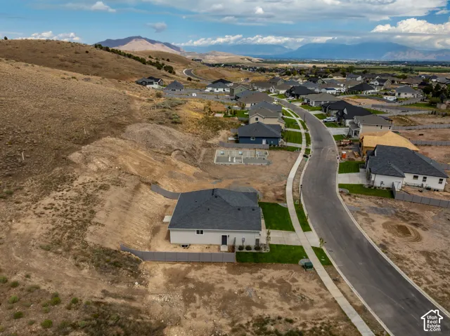 Aerial perspective of a residential property featuring a dark-shingled roof, attached concrete driveway, perimeter fencing, and expansive mountain scenery