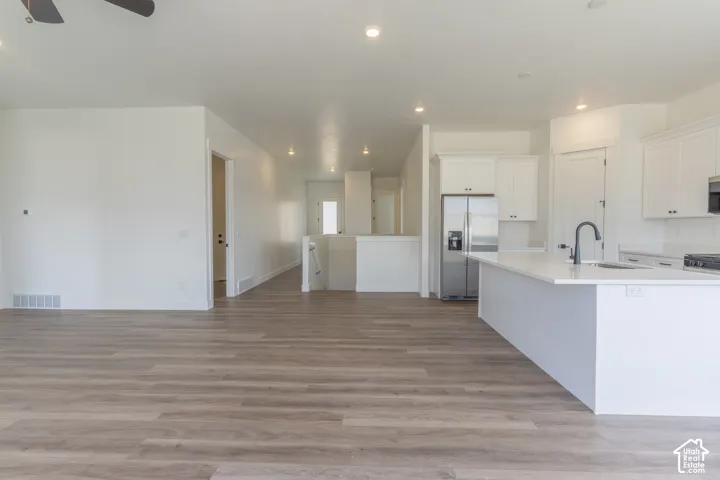 Open-concept kitchen featuring white shaker-style cabinetry, quartz countertops, a kitchen island with an undermount sink, and wood-finish flooring