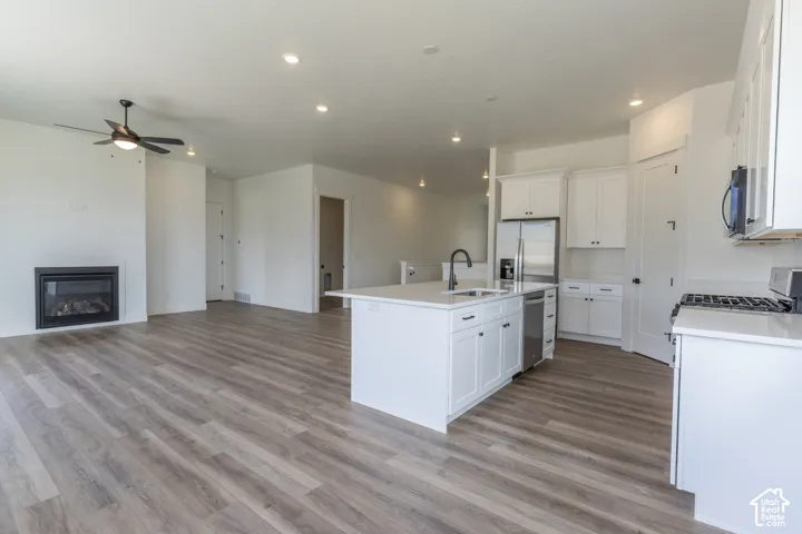 Kitchen featuring white cabinetry, center island with stone-composite countertop and undermount sink, stainless steel appliances, and built-in fireplace with black surround