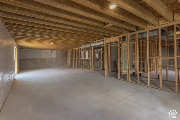 Unfinished interior space featuring exposed wood-stud framing, concrete flooring, exposed floor joists, and polyethylene vapor barrier wall sheeting