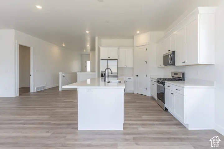 Kitchen featuring white cabinetry, an island with a sink, stone-finish countertops, stainless steel appliances, and wood-finish flooring