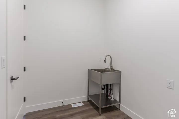 Stainless steel utility sink with a high-arch pull-down faucet on a metal stand, set against a wood-finish floor