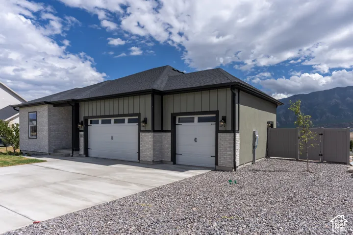 Exterior featuring vertical siding, masonry accents, a two-car garage, concrete driveway, and mountain backdrop