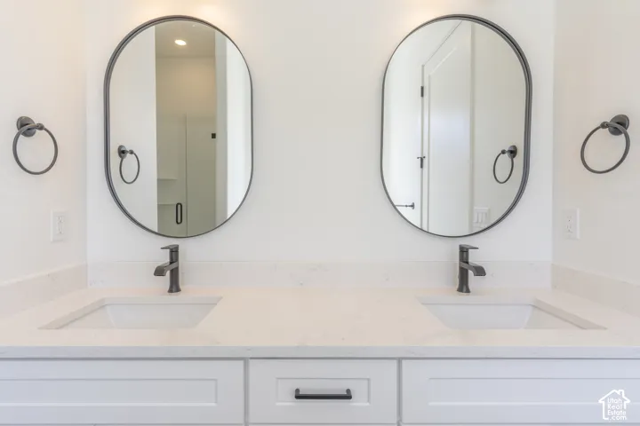 Dual-sink vanity featuring quartz countertops, undermount rectangular basins, matte black fixtures, and oval-framed mirrors