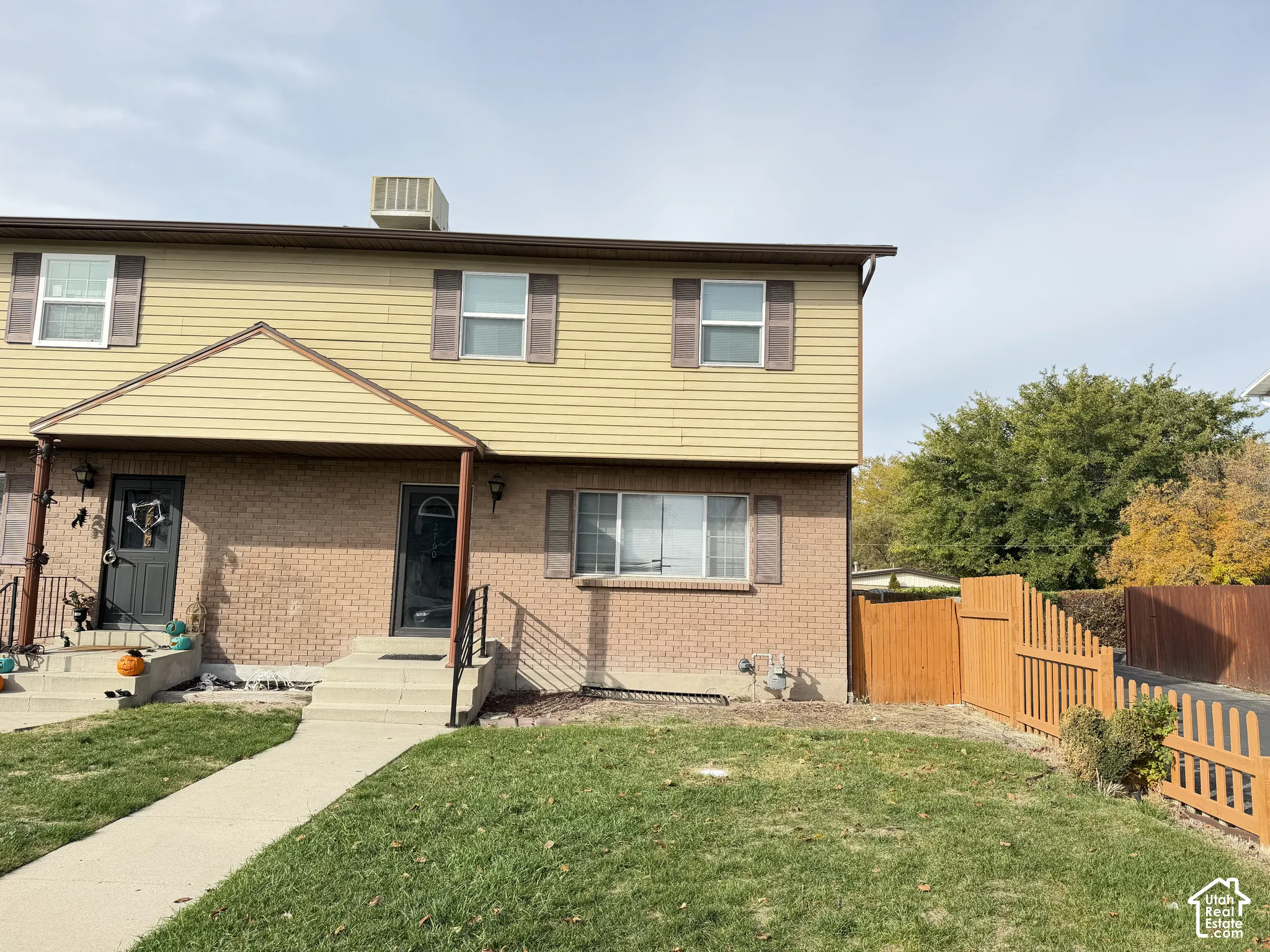 Two-story exterior featuring tan horizontal siding, brick masonry, wooden shutters, and a wood-slat privacy fence