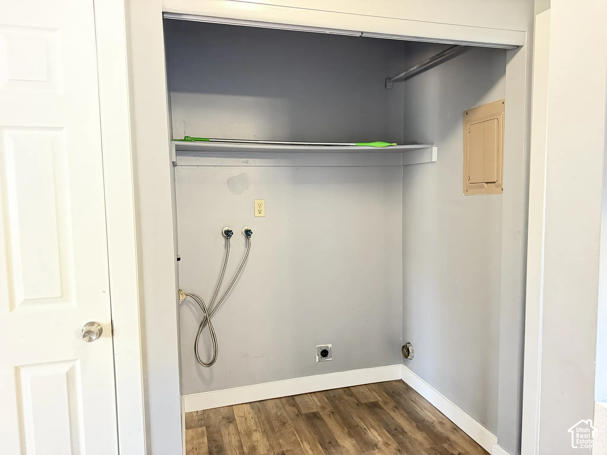 Utility alcove featuring wood-finish flooring, a built-in overhead storage shelf, a dedicated clothing rod, and water hookups