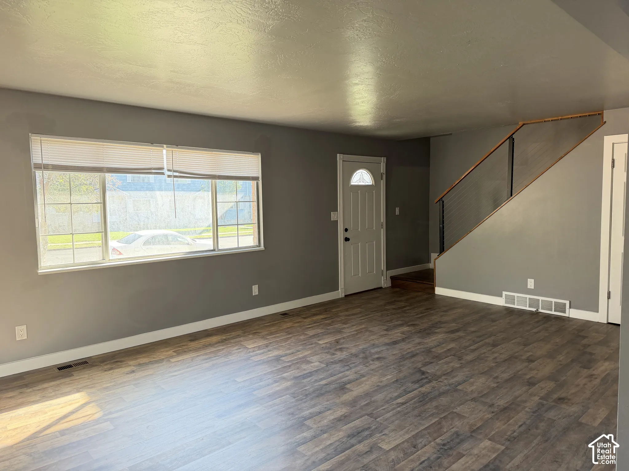 Interior space featuring wood-finish flooring, a large picture window with grid detailing, and a staircase with a horizontal cable railing system