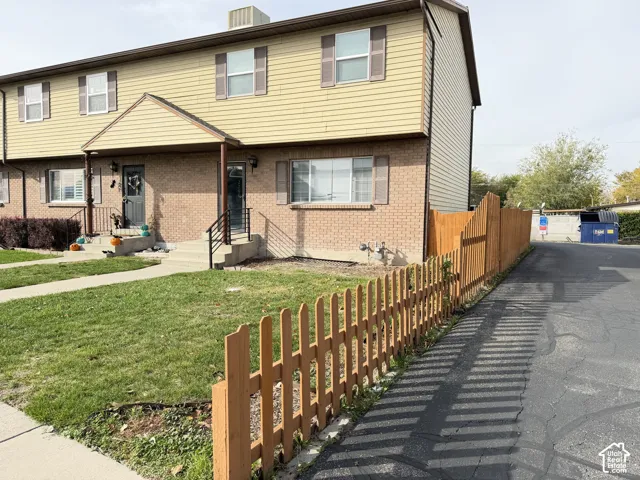 Multi-story exterior featuring a combination of brick masonry and horizontal siding, accented by window shutters and a wood-picket fence