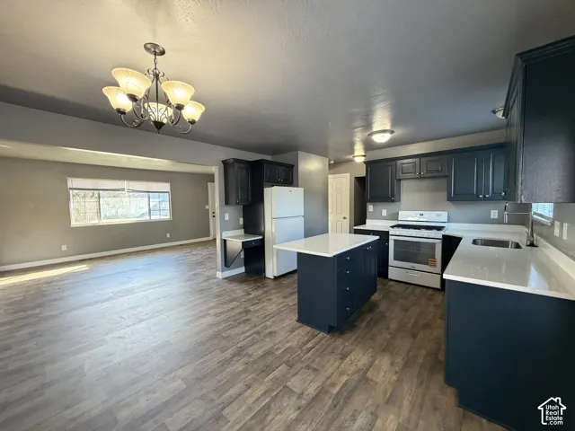 Kitchen featuring dark cabinetry, a central island with a solid surface countertop, wood-finish flooring, and a decorative multi-light chandelier