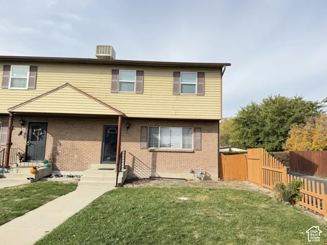 Two-story exterior featuring tan horizontal siding, brick masonry, wooden shutters, and a wood-slat privacy fence