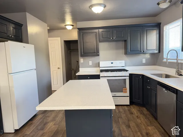 Kitchen featuring charcoal-toned cabinetry, white stone-composite countertops, a central island, wood-finish flooring, and stainless steel integrated appliances