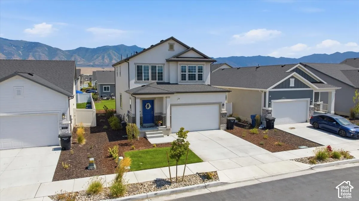 Two-story residence featuring a composite shingle roof, stucco exterior, two-car garage, concrete driveway, and mountain backdrop