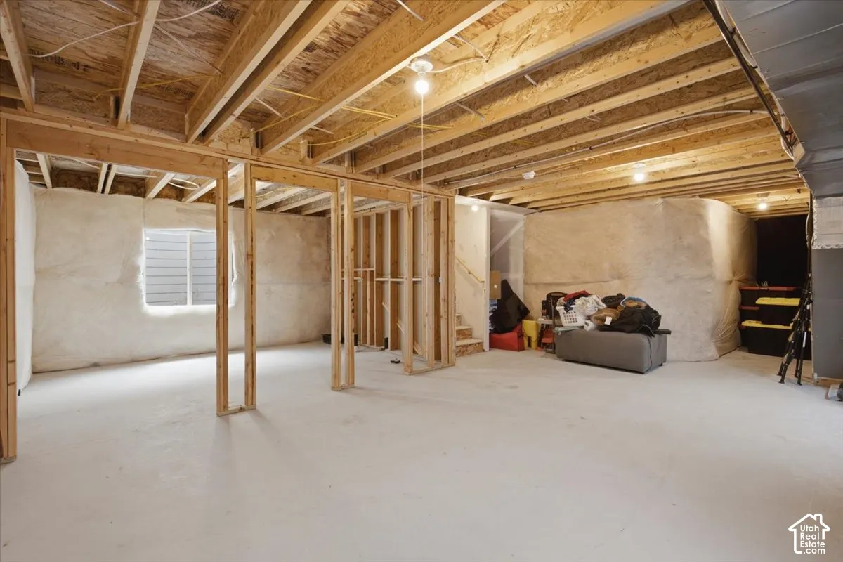 Unfinished lower level featuring exposed wood-stud framing, concrete flooring, exterior-grade window, and batt insulation