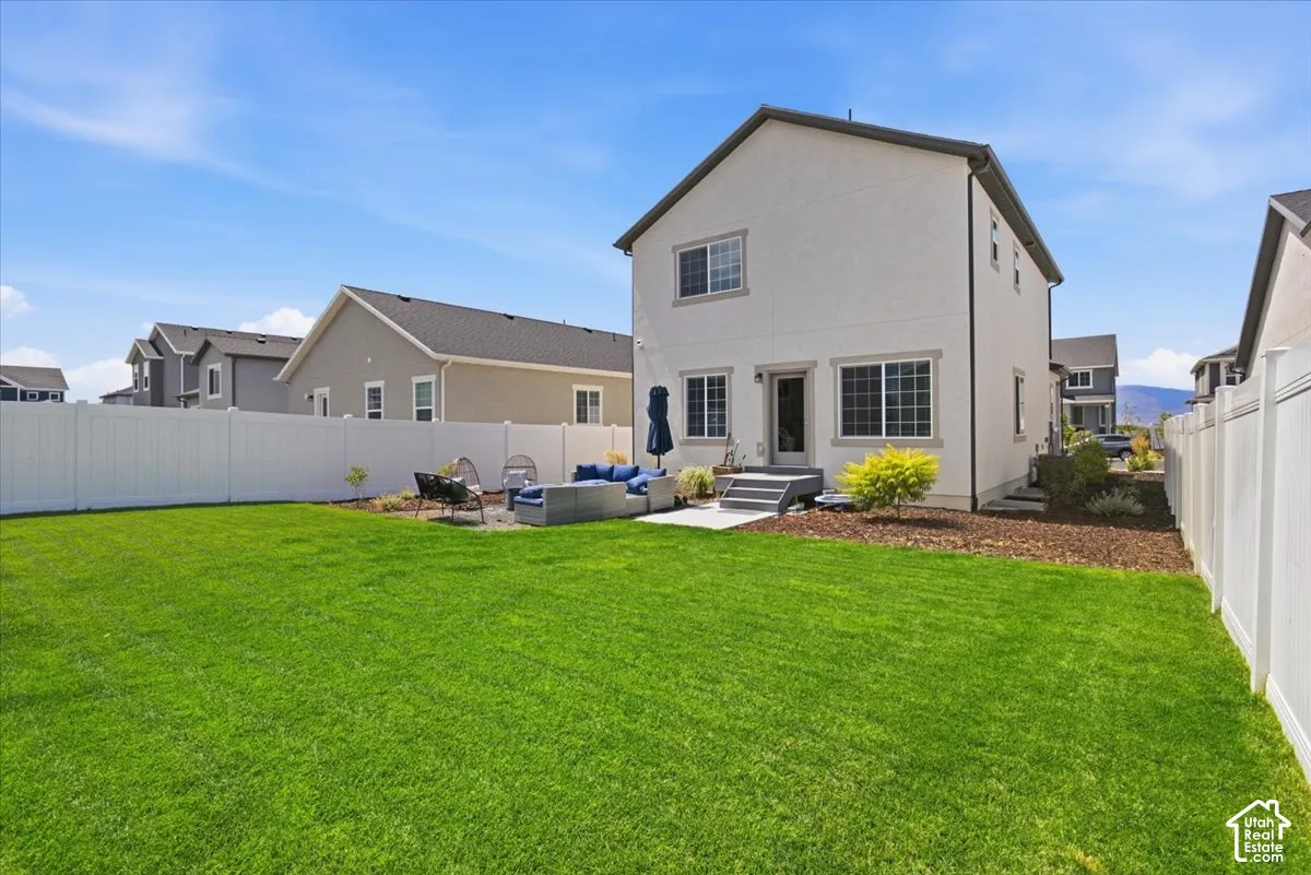 Backyard featuring a manicured lawn, full-perimeter white vinyl fencing, concrete rear patio, and exterior landscaping beds