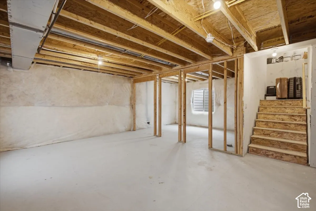 Unfinished interior space featuring exposed wood-stud framing, concrete flooring, insulated walls, and wooden staircase
