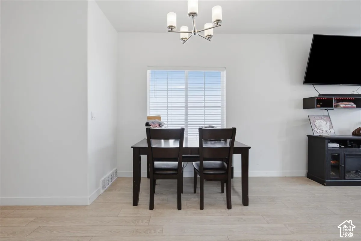 Neutral-toned wood-finish flooring, central five-arm chandelier with glass shades, and a single-pane window with horizontal blinds
