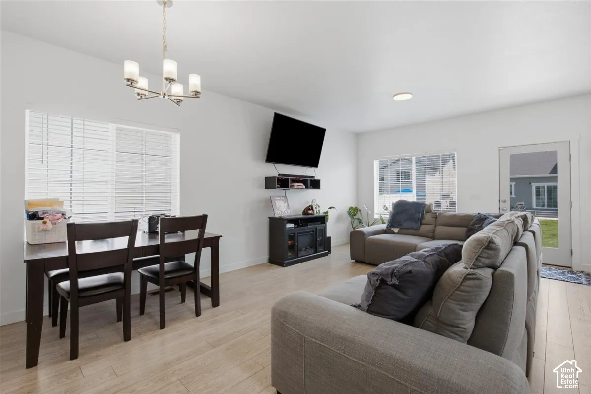 Open-concept interior featuring light wood-finish flooring, multi-pane windows with horizontal blinds, a five-light chandelier, and a glass-paneled exterior door