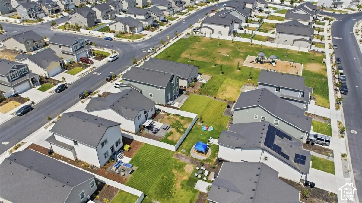 Aerial perspective of a residential neighborhood featuring paved streets, multi-level homes with pitched roofs, fenced rear yards, and an integrated communal playground