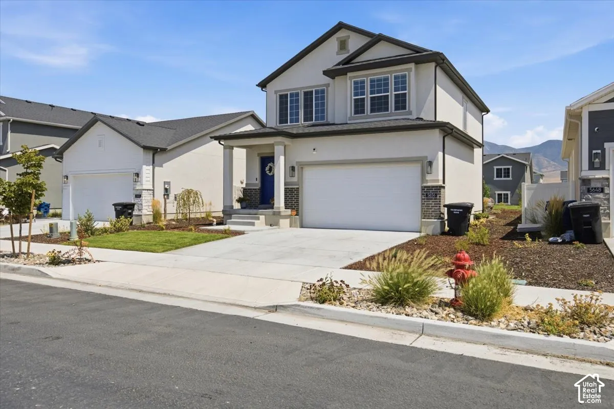 Two-story exterior featuring a stucco facade, stone veneer accents, a covered front porch with columns, a two-car garage, and concrete driveway