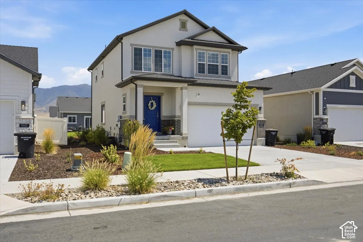 Two-story exterior featuring a neutral stucco facade, stone veneer accents, an attached two-car garage, and a covered front entryway