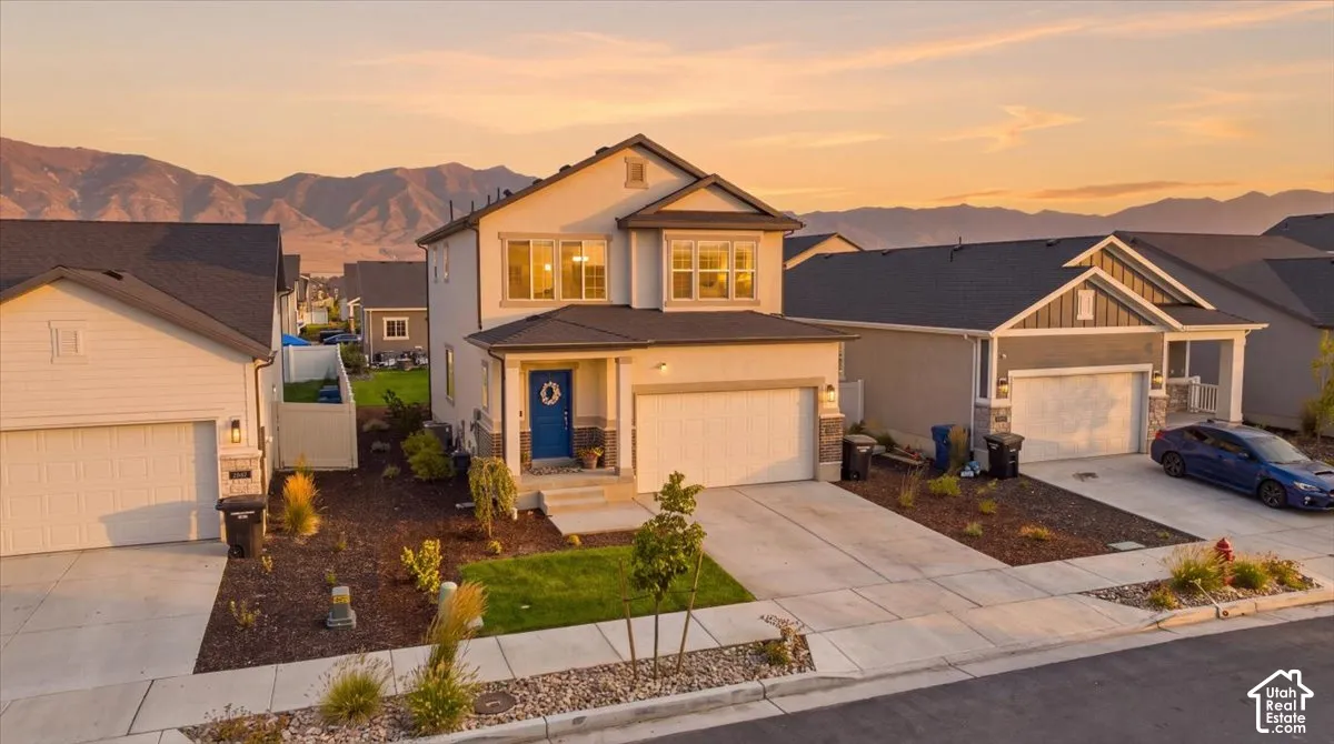 Two-story residence featuring a stucco and stone veneer exterior, an attached two-car garage, concrete driveway, and a mountain backdrop